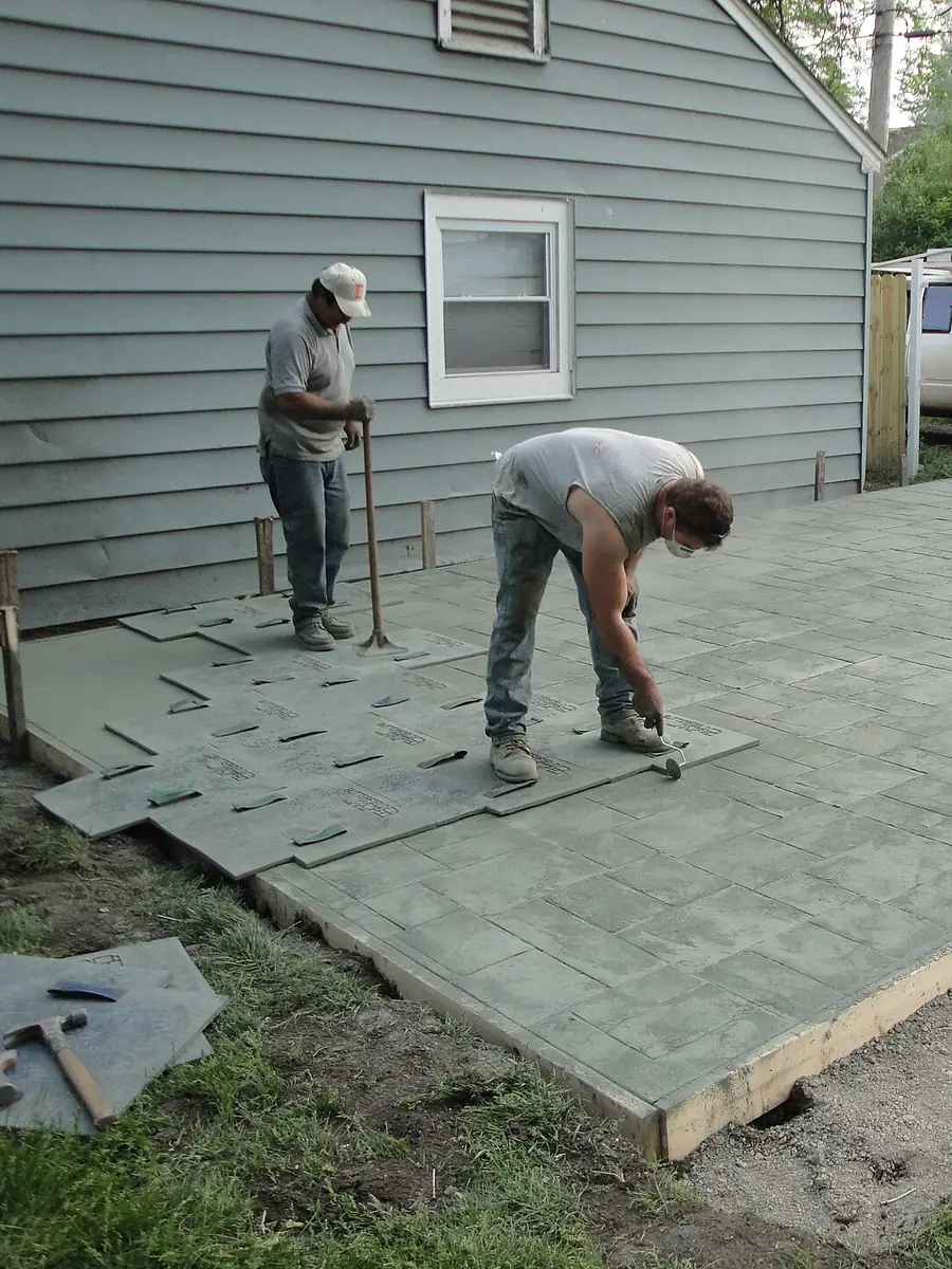 Crew stamping a freshly poured concrete patio beside a house